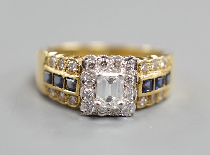 A modern 18ct gold, emerald and round cut diamond set square cluster ring, three three row sapphire and diamond set shoulders, size M, gross weight 6.6 grams.
